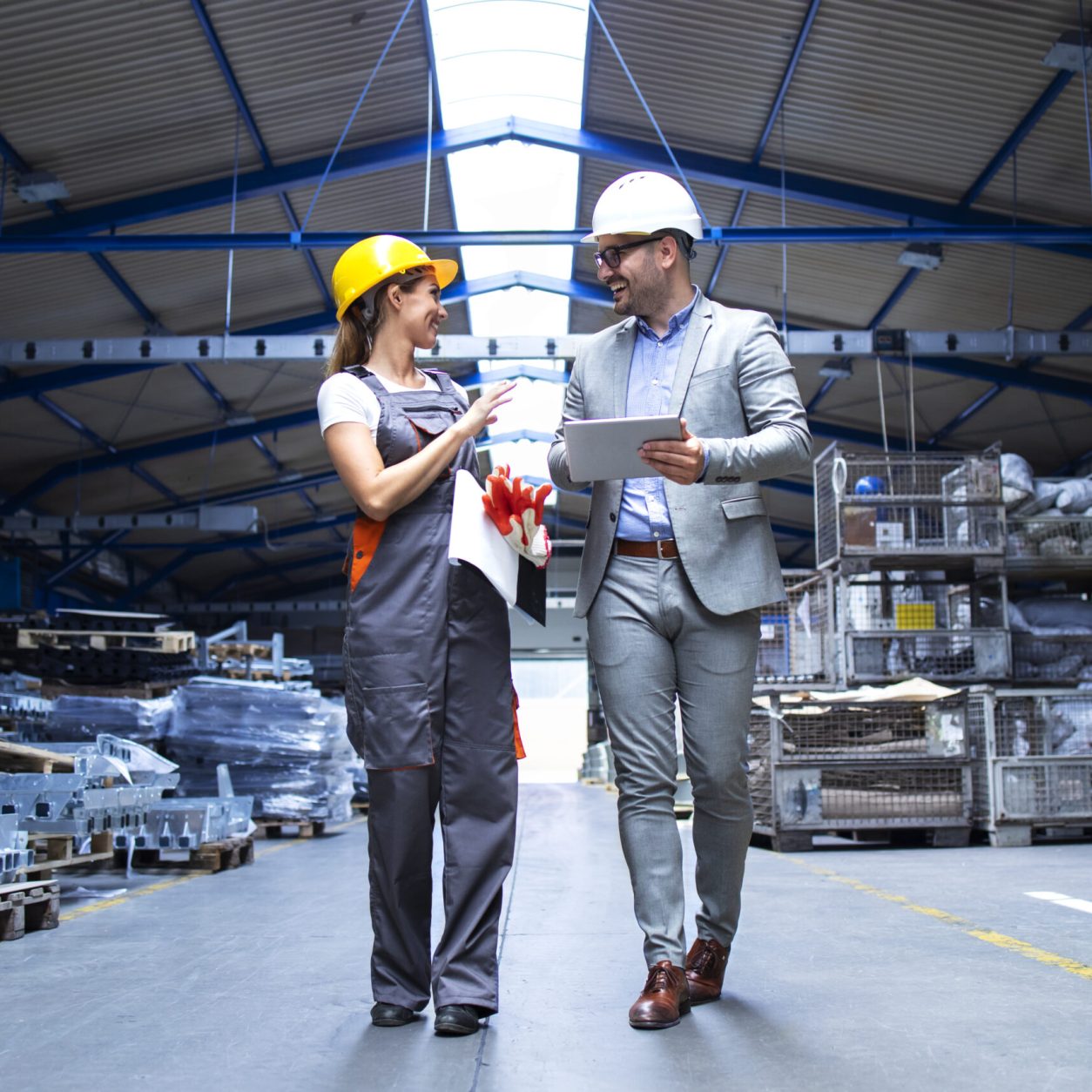Manager supervisor and industrial worker in uniform walking in large metal factory hall and talking about increasing production.